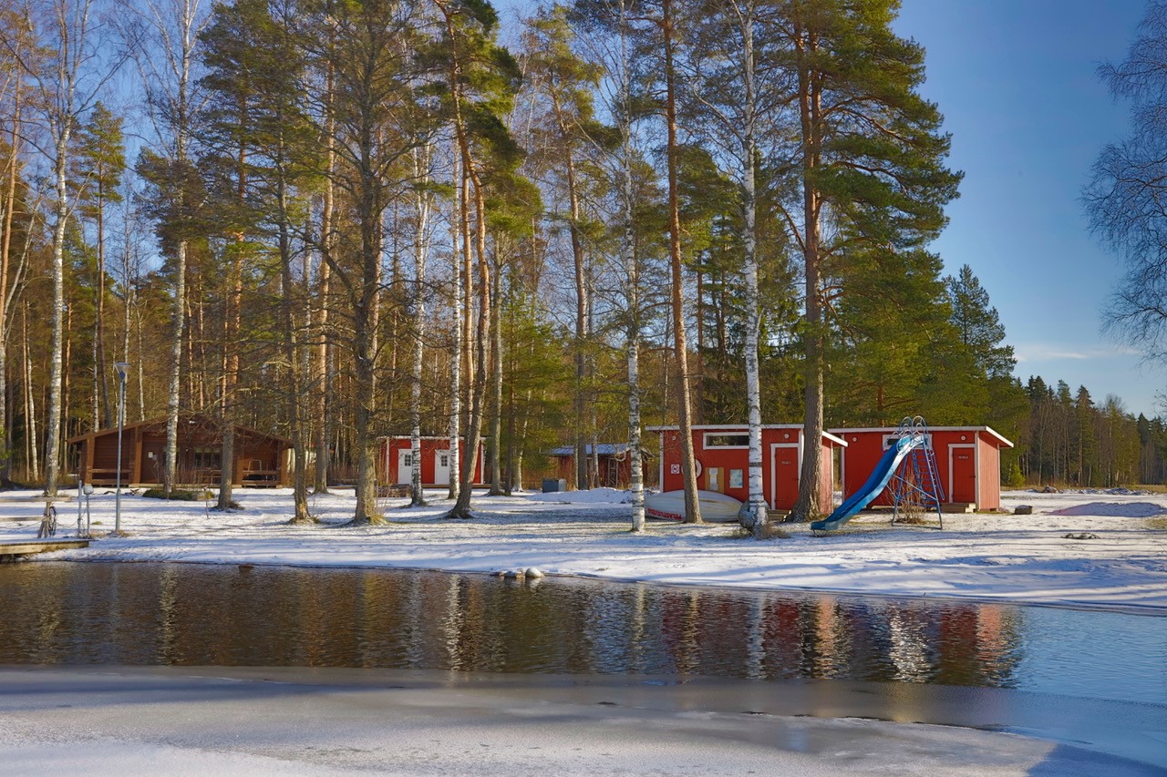 kuvassa talvinen Liipolanjärvi laiturilta kuvattuna, rannassa näkyy punaiset puiset rakennukset, sininen liukumäki ja kunnan saunarakennus